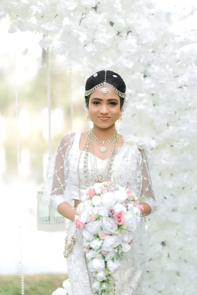 Bride in white holding a cascading bouquet in front of a wall of white blossom