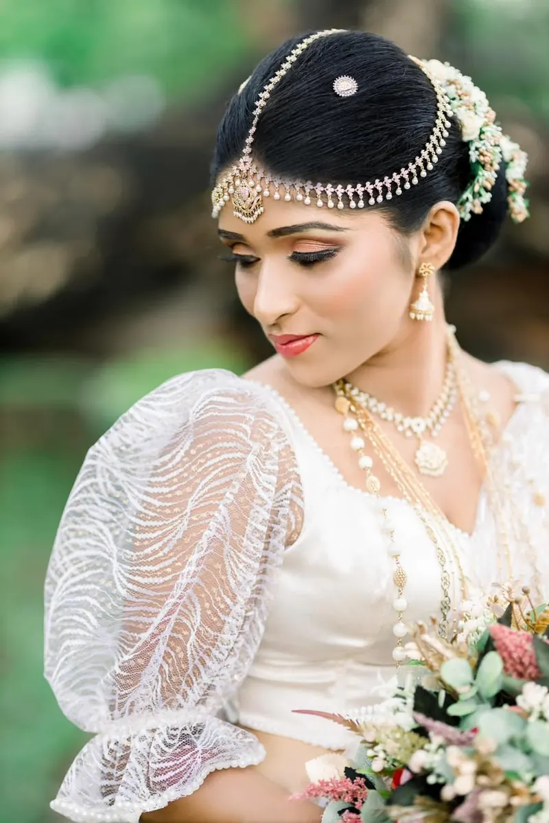 Bride in a sheer embroidered blouse holding a pink and green bouquet