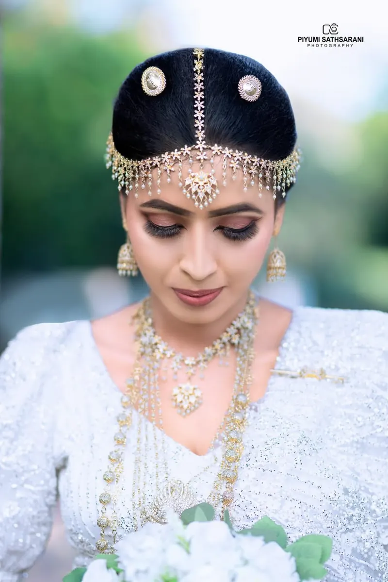 Bride in a pearl and gold headpiece looking down, in a garden