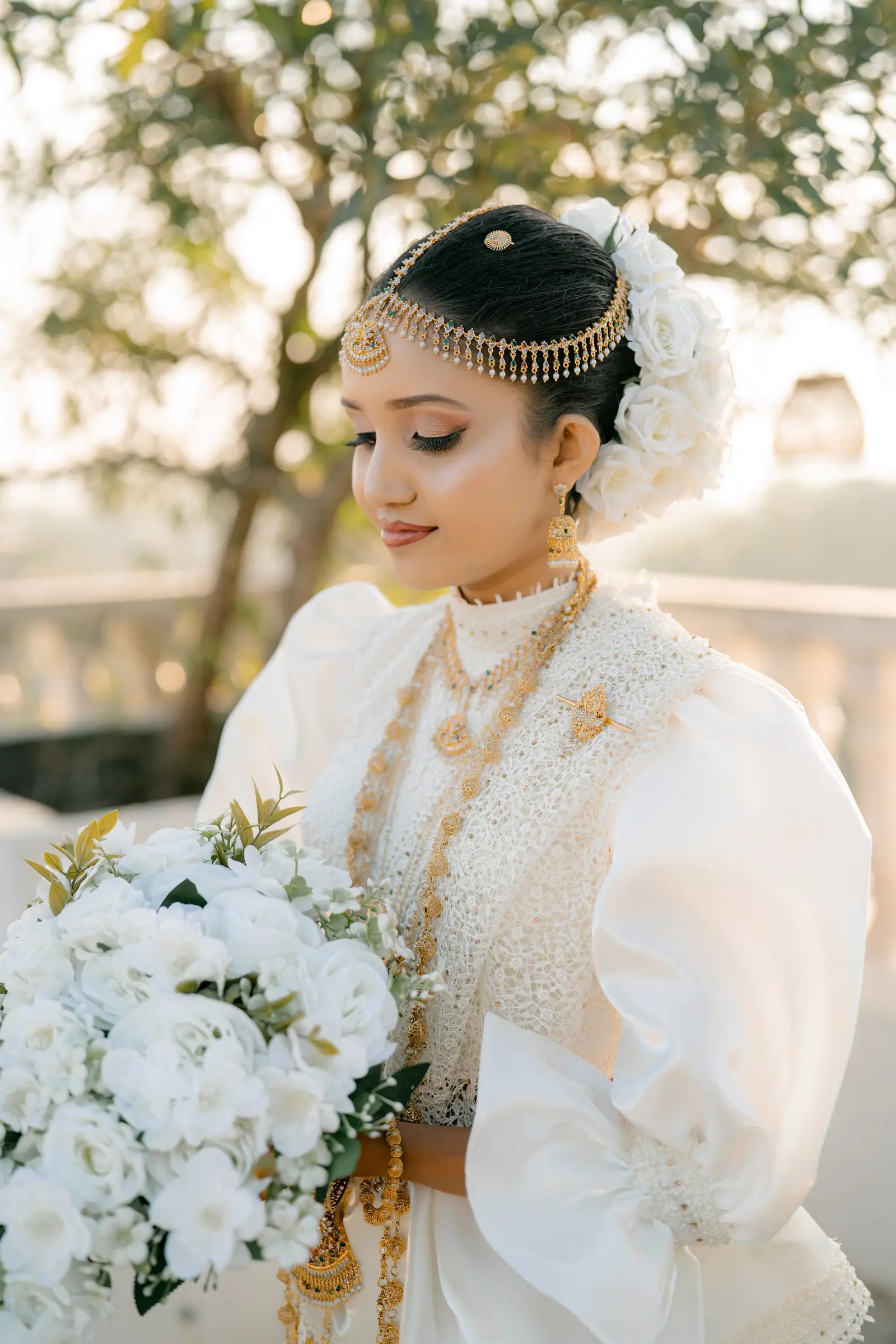 Bride looking down at a white rose bouquet on a terrace at golden hour