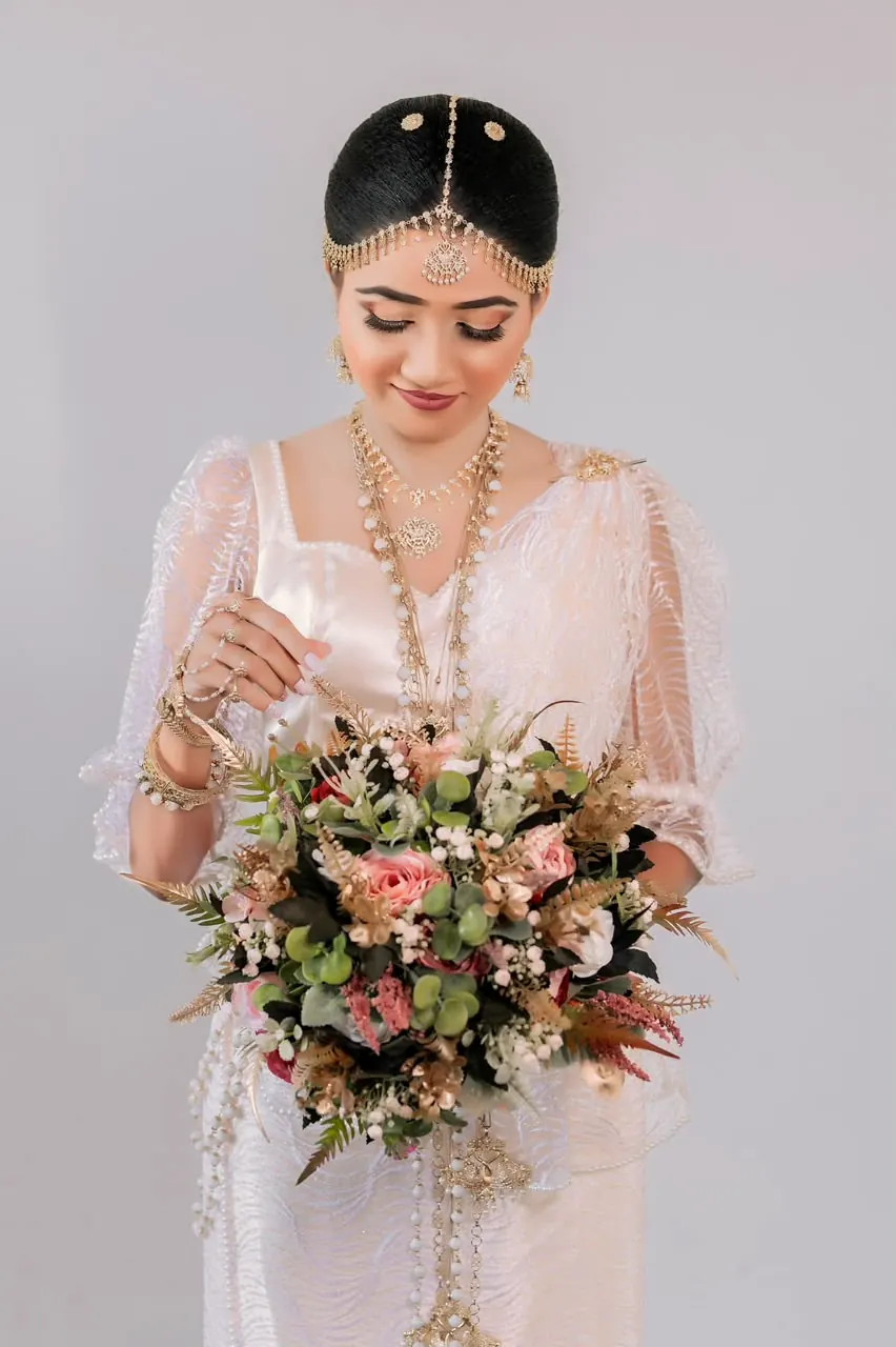 Bride holding a bouquet with layered gold necklaces, lilac backdrop